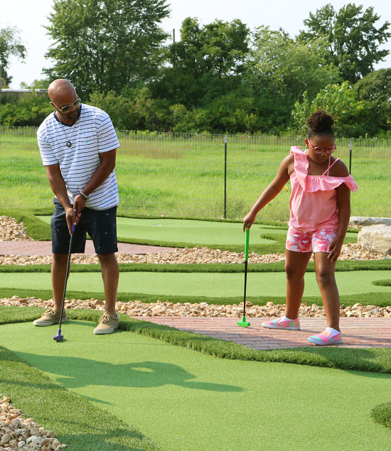 Dad putting while his daughter watches on the putt putt St. Louis course
