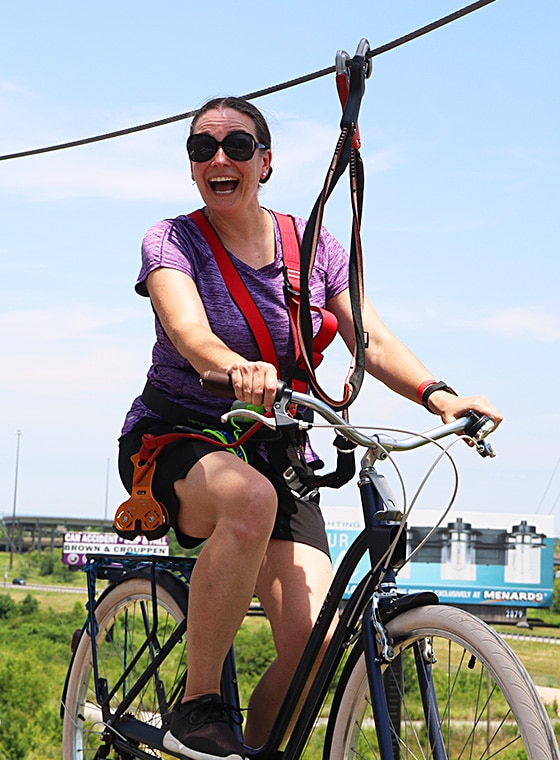 a mom on a bike on a beam smiling as she crosses the high ropes course in St Louis