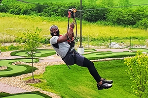 man smiling on the zipline with the miniature golf course in the background