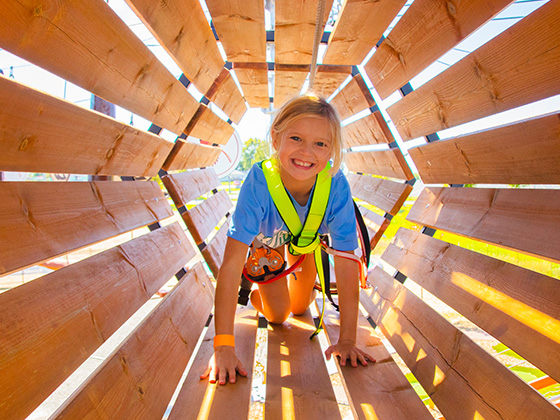 Smiling Girl crawling through the tunnel on ropes course